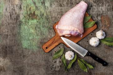 Raw turkey thigh with spices and garlic on a wooden board. Top view of a turkey, a knife on a vintage wooden background. Culinary background.