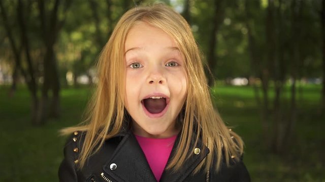 Lovely little blonde girl wearing a leather jacket is closing her eyes with her palms and opening them. She is astonished. Handheld real time establishing shot