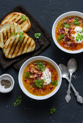 Smoked paprika lentil soup with grilled cheese sandwiches and crispy bacon on a dark background, top view. Delicious comfort food concept. Flat lay