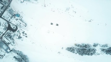 Aerial top down view of two snowcats or snow groomers on a mountain ski slope