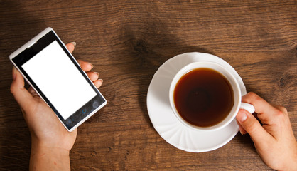 Female hands with mobile phone and cup of tea on wooden background. top view