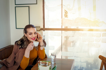 smiling girl in a cafe drink coffee and speaking on smartphone .