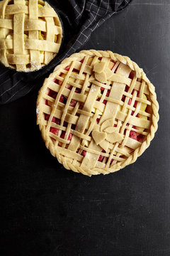 Pie crust design ideas - various ways of pie decoration with lattice and leaves. Apple, strawberry and raspberry pies uncooked on black table.