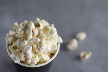 Popcorn in black paper cup on a gray background.