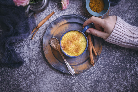 Woman drinking golden milk turmeric latte served in a blue cup
