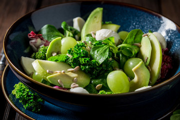 Kale salad with avocado, lettuce and grape in blue bowl