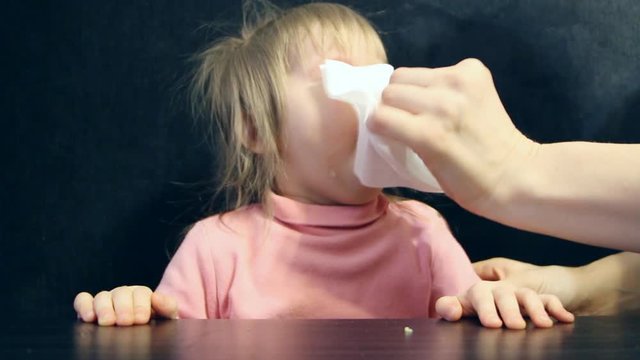 Mom with a crying child in his hand with a handkerchief wipes his snot