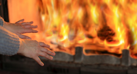 Ogień w kominku, kobieta grzeje dłonie.