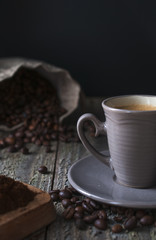 Coffee cup on wooden table with roasted beans and coffee powder