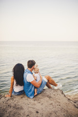 Theme family vacation with small child on the nature and sea. Mom, Dad and daughter of one year are sitting in embrace, girls in the hands of man, with his back at height of cliff overlooking the sea