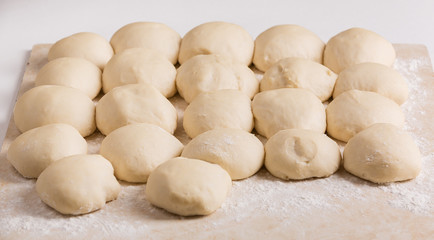 Ball-shaped dough pieces sprinkled with flour prepared for pies making on the table
