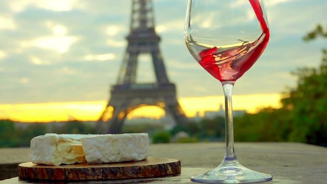 Red wine is poured into a glass. Piece of Camembert cheese with a wooden board. The Eiffel Tower. Sunset