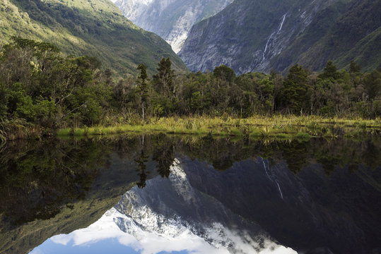Paisaje de picos de montañas nevados y verdes con cielo nublado reflejado en un lago  en Nueva Zelanda