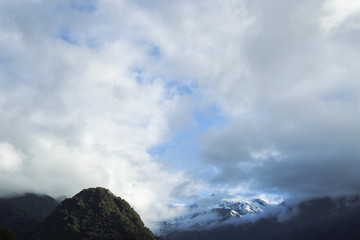 Paisaje de picos de montañas nevados y verdes con cielo nublado en Nueva Zelanda