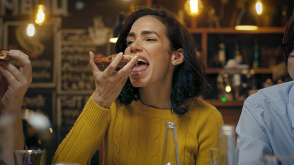 Beautiful Hispanic Woman Eats Pizza Slice at the Stylish Restaurant. She's Surrounded by Her Friends.