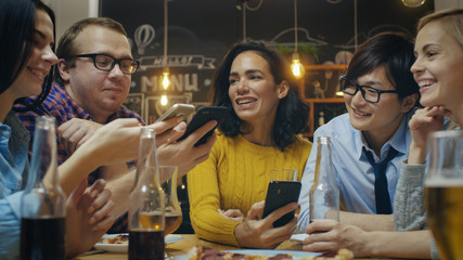 In the Bar/ Restaurant Diverse Group of Friends Have Good Time Sharing Pictures and Whatnot with Their Smartphones. Beautiful People in Stylish Establishment.