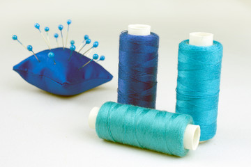 blue threads on reels pincushion for needles selective focus, white background