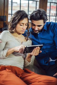 Young Couple Sitting On Sofa Using Digital Tablet