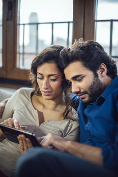 Young Couple Sitting On Sofa Using Digital Tablet