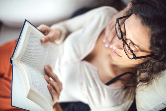 Young woman reading a book while lying on sofa