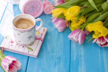 Fototapeta na wymiar Spring morning, fragrant coffee and tulips of yellow and pink color. Donuttsy copies. Blue wooden background, place for text and postcard.