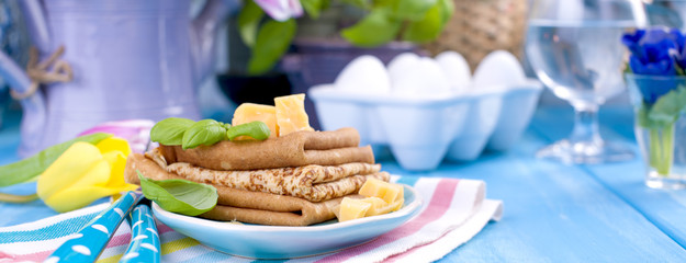 Homemade traditional pancakes with parmesan and basil for spring carnival. Italian breakfast. Bright flowers of tulips. Blue background. A free place for text or a postcard.