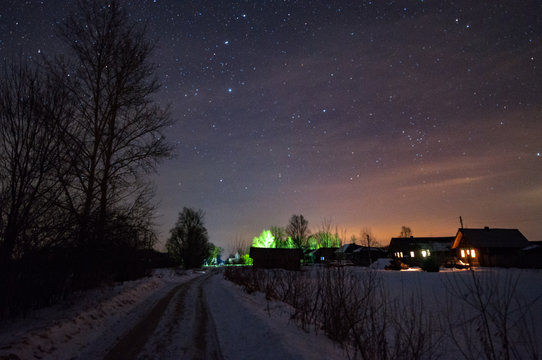 The Road In Russian Village , Frosty And Snowy At Night. The Trees And The Starry Sky Overhead. The Constellation Of The Great Bear Shines In The Sky.