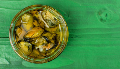 Marinated mussels in a glass jar on a green wooden background.