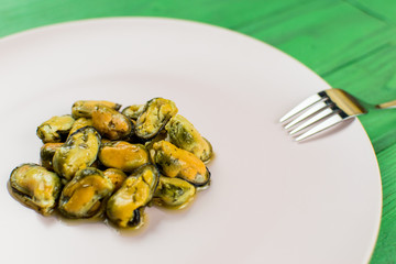 Mussels on a pink-lilac-colored plate on a wooden green background.