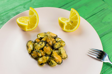 Mussels on a pink-lilac-colored plate on a wooden green background.