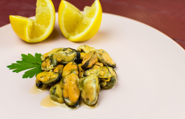 Mussels on a pink-lilac-colored plate on a wooden dark red background.