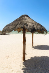Two palapa shades with shadows on whitle sand beach with ocean in background