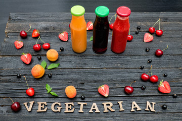 Three bottles with juice, fruit and inscription Vegetarian on black wooden background. Food concept