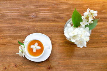 Obraz na płótnie Canvas White mug of green tea and a vase with jasmine. Wooden table. Top view