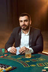 A young man in a business suit sitting at the poker table. Man gambles. The player at the gaming table playing cards.