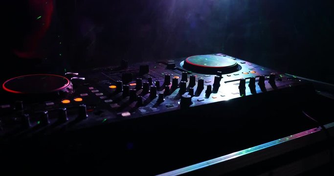 DJ Spinning, Mixing, and Scratching in a Night Club, Hands of dj tweak various track controls on dj's deck, strobe lights and fog, selective focus, close up. Slider Shoot