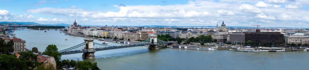Obraz premium Wide panorama of Budapest with visible bridges, ships on the river and historic buildings and the parliament building on a summer sunny day
