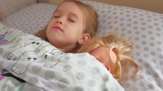 Adorable little girl sleep in the sofa bed and hug her baby doll.