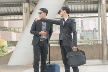 Young businessmen pointing the way to stranger man who was meet on the street.Young businessman wearing a suit and sunglasses with bag drag ask for directions from strangers.lifestyle concept.