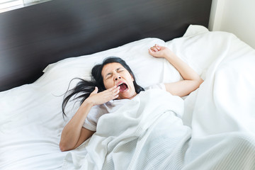 Fototapeta na wymiar Asian woman stretching and yawning or gape feeling lazy on bed after wake up in the morning
