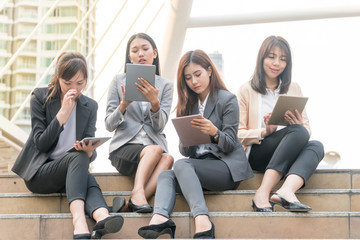 Group of business women are watching the tablet of their own interests and do not talk to each other in a modern city. Beautiful young woman wearing the business suit using tablet on the stairs.