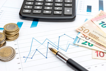 Euro bills and coins with calculator and pen on the business graphs. Financial background.