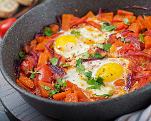 Fried eggs with pieces of pumpkin, red onions and tomatoes. Tasty breakfast.