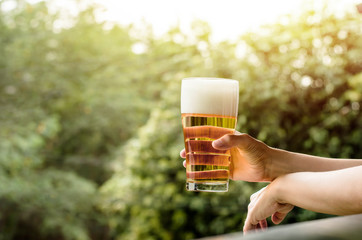 Drinking Beer in Summer Concept. Woman with Glass of Beer on Balcony. Natural Sunlight and Tree as...
