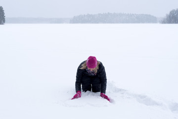 Fototapeta na wymiar A woman on a frozen lake drawing heat shape to the snow