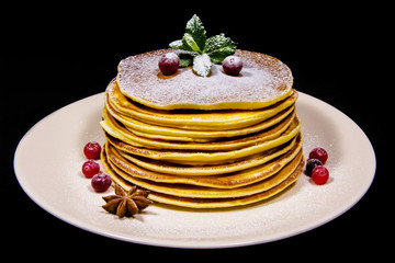 Fresh pancakes on a white plate sprinkled with sugar powder on them lies the cranberry and mint next to the bowl plate