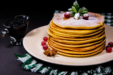 Stack of Pancakes on a white plate with green wipe cranberry puddings and cinnamon sprinkled with sugar powder along with blueberry jam and a glass of milk