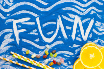 Fun inscription on a blue colored sand with waves, candies, orange, top view, flat lay