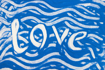 Love inscription on a blue colored sand with waves, top view, flat lay