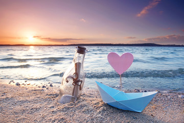 Flaschenpost und Papierboot am Strand